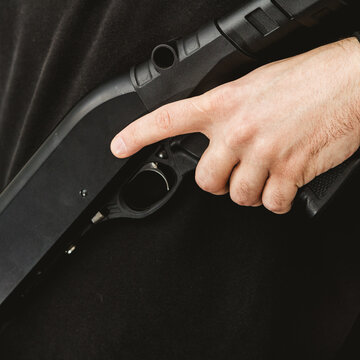 Close up of male hand gripping black shotgun with finger on trigger guard