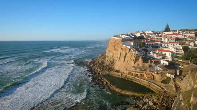 The video shows a panoramic view of Azenhas do Mar, a fishing village in Portugal. It sits on a cliff overlooking the Atlantic Ocean with waves breaking against the rocks.