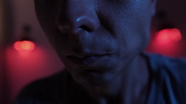 Close up of an angry man with tense lips and clenched jaw, suppressing intense anger and emotional frustration through restrained facial expression in dramatic red and blue low key lighting