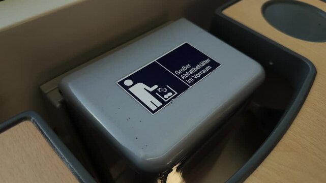 Kleine Muelleimer am Tisch eines Fahrgastsitzes in einem deutschen Zug. Detail des Abfallbehaelters mit Aufkleber im Innenraum eines modernen Zuges der Deutschen Bahn.