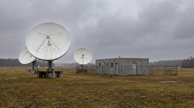 Satellite ground station with large parabolic antenna dishes and an equipment building in a flat field