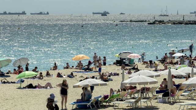tourists on beach in barcelona and container ships on the hoirizon