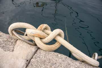 Fototapeta premium Braided mooring rope tied in a knot on a steel pier ring in morning harbor.