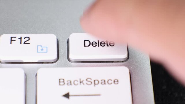 Close-up view of a finger pressing the Delete key on a white computer keyboard, highlighting the action of removing text or files.