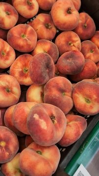 Fresh flat peaches displayed in baskets at a market or supermarket. The video shows how to identify ripe and high-quality flat peaches by examining their color, texture, and firmness.