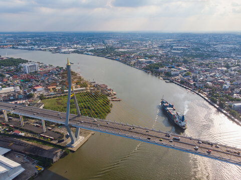 Aerial drone view of Kanchanaphisek cable-stayed bridge over Chao Phraya river with cargo container ship in Bangkok Thailand