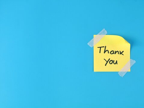 Thank you handwritten text on a yellow adhesive note secured with adhesive tape on blue background with copy space. Perfect for business appreciation, customer service, gratitude, and message concepts