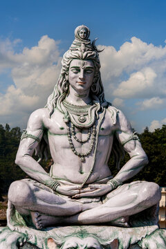 Lord Shiva statue meditating in lotus pose. Statue of Hindu god Shiva sitting in meditation pose. Religious landmark and spirituality concept on beautiful blue sky and clouds background