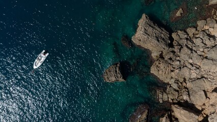 Aerial view of a yacht or boat in green sea by the coast with rocks © raeva