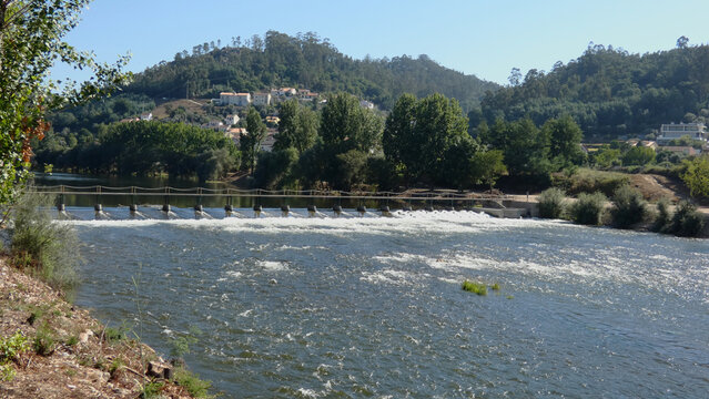 White water flowing over a river weir below green hills in Portugal
