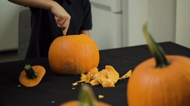Removing seeds and cleaning inside of jack o lantern pumpkin in close up shot, child hands scooping fibrous pulp for halloween celebration preparation in October
