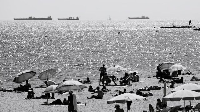 tourists on beach in barcelona and container ships on the hoirizon