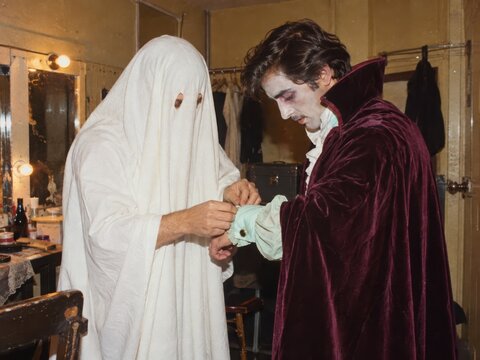 Backstage photograph of two adults in ghost and vampire costumes fastening an oversized mint cuff