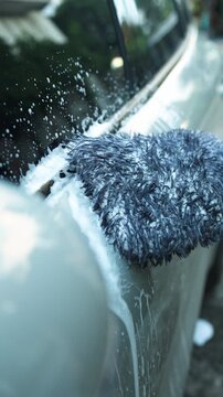 Close-up of hand washing soapy car side door with soft microfiber wash mitt. DIY auto detailing, car care and vehicle maintenance lifestyle concept. Vertical Shot