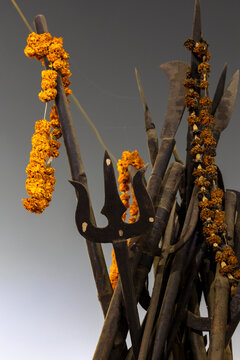 Iron tridents and spears decorated with orange marigold garlands against a grey sky at the Maha Kumbh Mela, Prayagraj, India