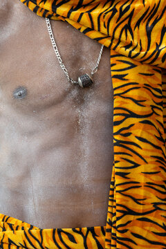 Close-up of the bare chest of a Naga Sadhu with ash a silver chain and a rudraksha bead beside a tiger print cloth, Prayagraj, India