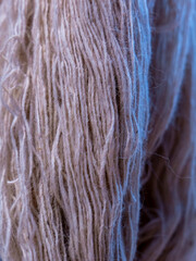 Close-up detailed abstract background of textured light pink or beige wool yarn fibers hanging vertically. © fornax