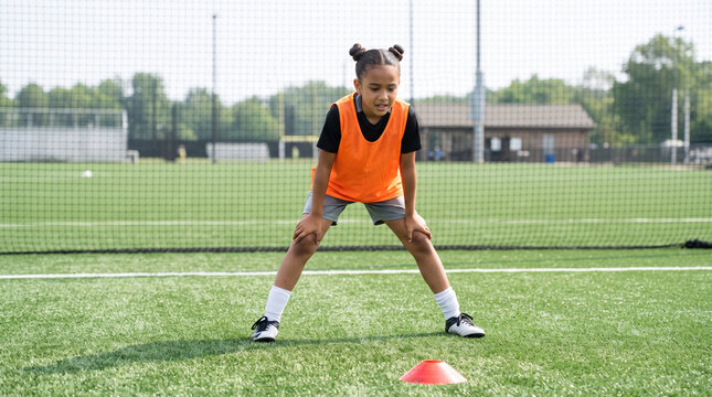 Young girl resting with hands on knees during soccer practice on turf field