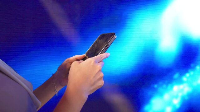 Hands hold and tap a black smartphone in front of a blue digital display, with luminous circles and flowing light patterns behind the device in a close cropped view of fingers using the touchscreen.