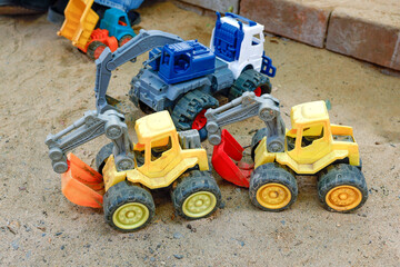 Colorful toy construction vehicles including dump trucks, bulldozers and tractors scattered in a sandy playground, outdoor play, childhood, imagination and learning through play © cgdeaw