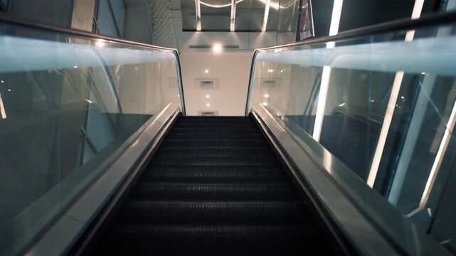 An empty escalator rises in slow motion between glass panels and metal handrails, with black steps leading toward a bright interior beneath rows of ceiling lights in a clean modern building in Taipei.