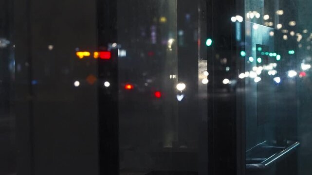 Slow motion captures distant headlights and colorful traffic lights beyond a dark window in Taipei, with circular bokeh behind the sharp outlines of a window handle, sill and vertical frames at night.