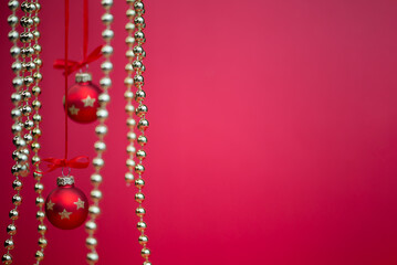 Red Christmas baubles and hanging golden bead garlands on a festive red background. Selective focus and blurred decorations create depth, with ample copy space for holiday greetings and advertising. © ольга дубровная