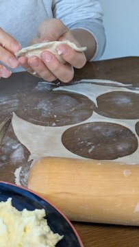 Woman hands making traditional pierogi dumplings at home kitchen table, rolling pin and raw dough preparing delicious homemade meal, authentic culinary workflow process for Polish cooking concept