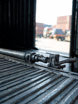 Industrial container terminal yard view from inside an empty cargo shipping container with corrugated metal walls and locking mechanisms.