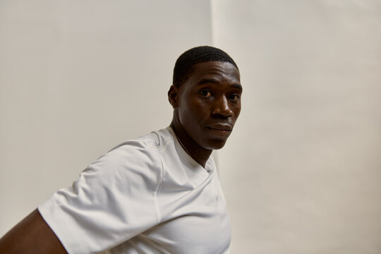 Man wearing a white shirt looks at the camera in a simple settin