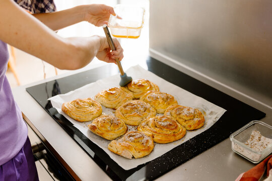 Woman brushing cinnamon rolls with egg before baking in a kitchen