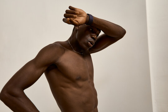 Man poses against a plain wall while wiping sweat from his brow
