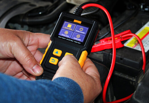 Hands holding a car battery tester designed to analyze the condition of batteries
