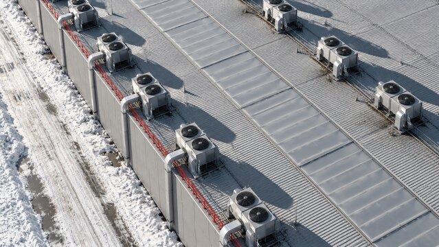 Aerial view of a modern data center roof with cooling systems, featuring ribbed grey metal and red rails for technical reports