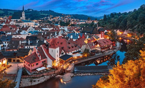 Czech Krumlov Czech Republic. Evening panorama old town illuminated street lamp over river Vltava. Picturesque landscape with authentic houses with red tegular roofs.