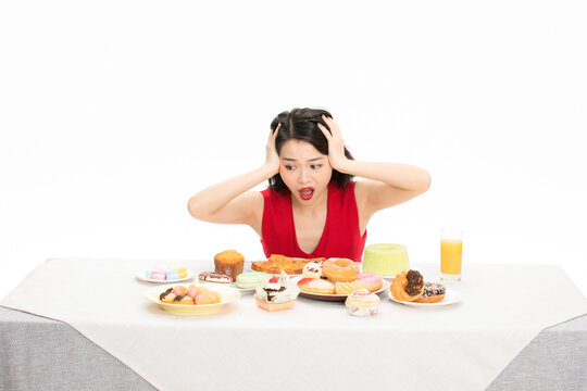 Shocked woman resisting temptation from a table full of sweets and desserts