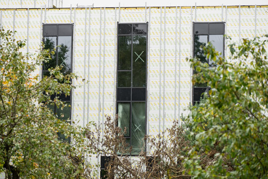 Unfinished building facade with tall installed windows, exposed membrane and vertical support rails, showing the exterior enclosure stage before final wall cladding installation