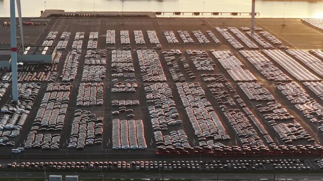 Aerial drone view of thousands of new import export cars parked in a sea port terminal. Commercial automotive supply chain and maritime freight logistics.
