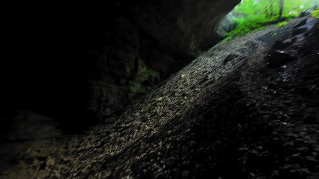 Viewpoint, to the mysterious entrance to the natural cave of Sakinule in Georgia with a rocky arch, lush green foliage and a path leading to the dark interior of the cave