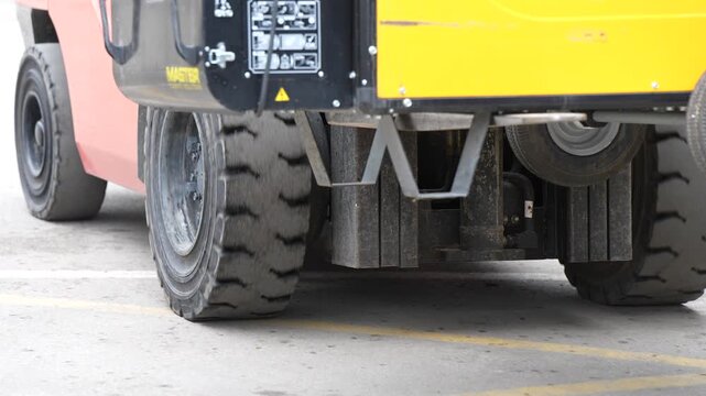 Industrial machinery wheels roll across a marked concrete floor beside exposed lower body components, showing vehicle movement during the transport of mounted equipment