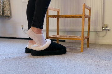 Person wearing cozy black fleece slippers and white ankle socks on a grey carpeted floor at home. © Kos6ka
