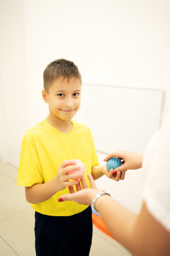 School age child participates in a sensory motor exercise with a therapist using textured therapy balls, developing hand coordination, motor planning and sensory processing skills.