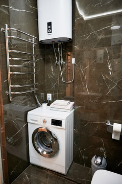 Laundry area in modern bathroom with washing machine, water heater and heated towel rail