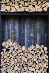 Fototapeta premium Chopped firewood stored in wooden rack against rustic wall. Stacked logs arranged in sections