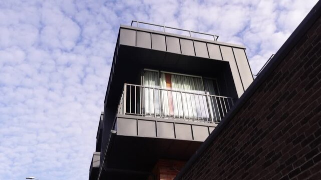 Low-angle shot of a contemporary apartment building's protruding balcony with metal railing and sheer curtains