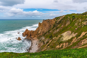 Fototapeta premium Cabo da Roca dramatic coastal cliff overlooking Atlantic Ocean in Portugal. Scenic westernmost point of Europe with rugged landscape, ocean waves and natural coastline.