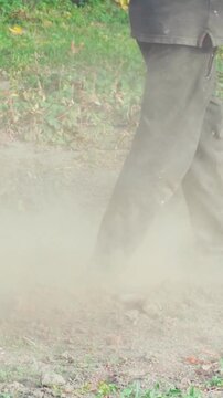 Agricultural tiller wheel moving across dry soil, rotating belt and metal engine stirring up a thick cloud of dust in a rural field setting