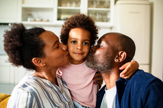 Parents kissing child on both cheeks in kitchen