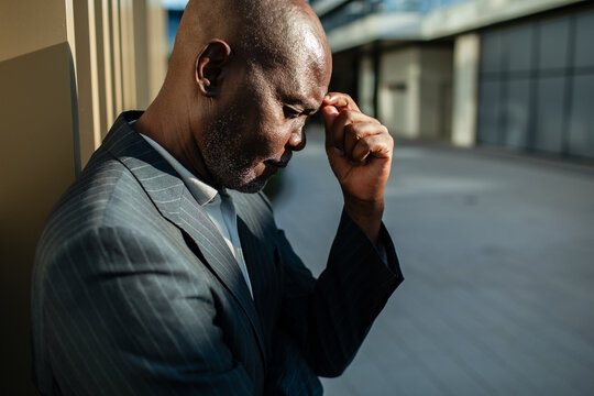 Businessman leans on wall and pinches the bridge of his nose