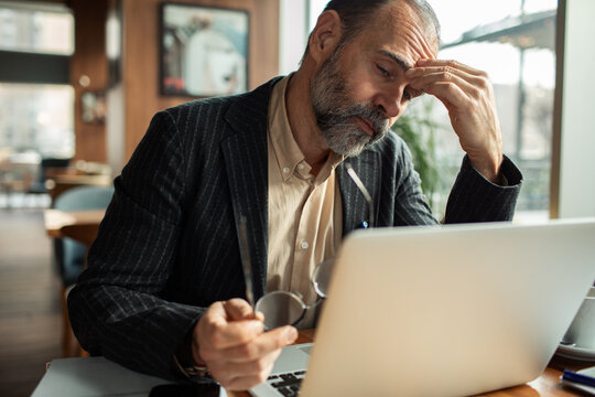 Stressed businessman rubbing forehead while working on laptop at cafe